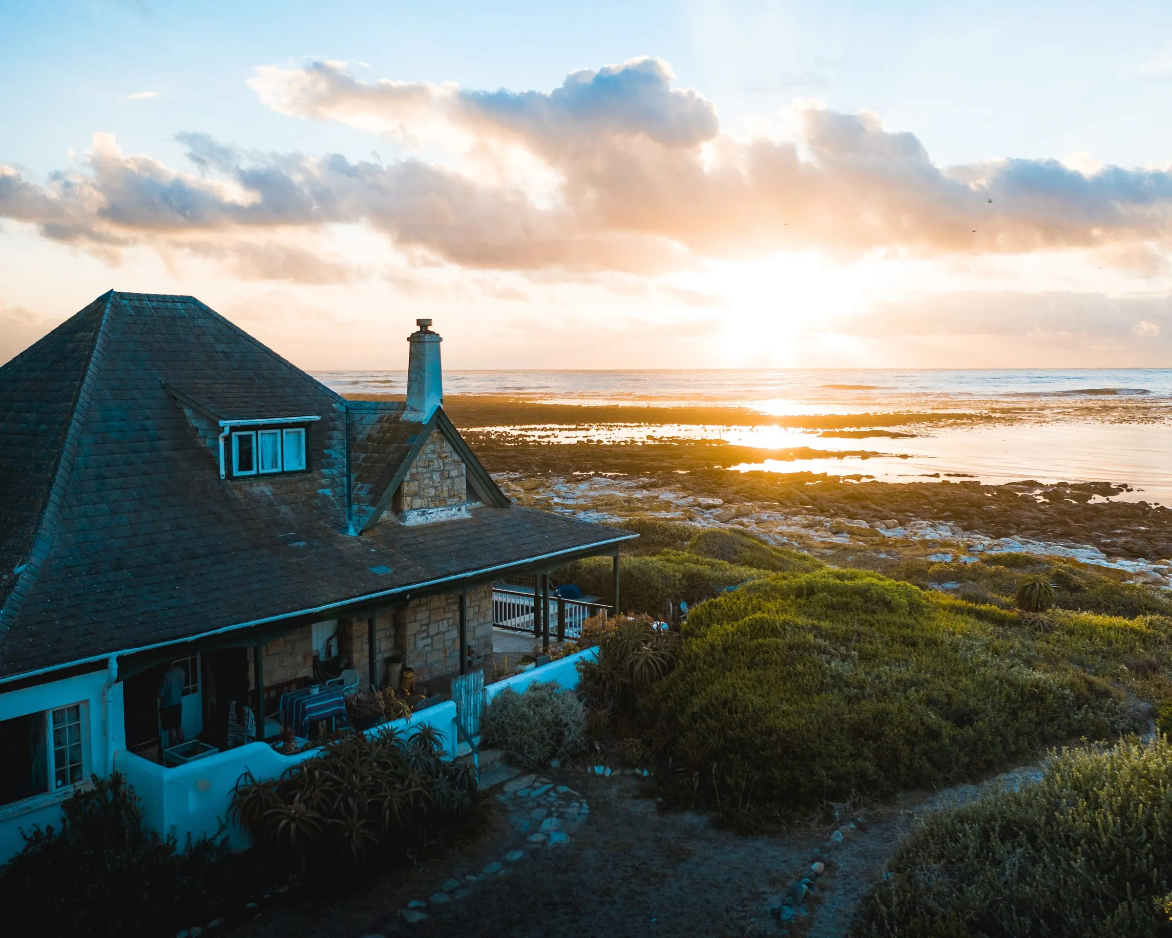 Casa frente al mar con el sol poniéndose en el horizonte