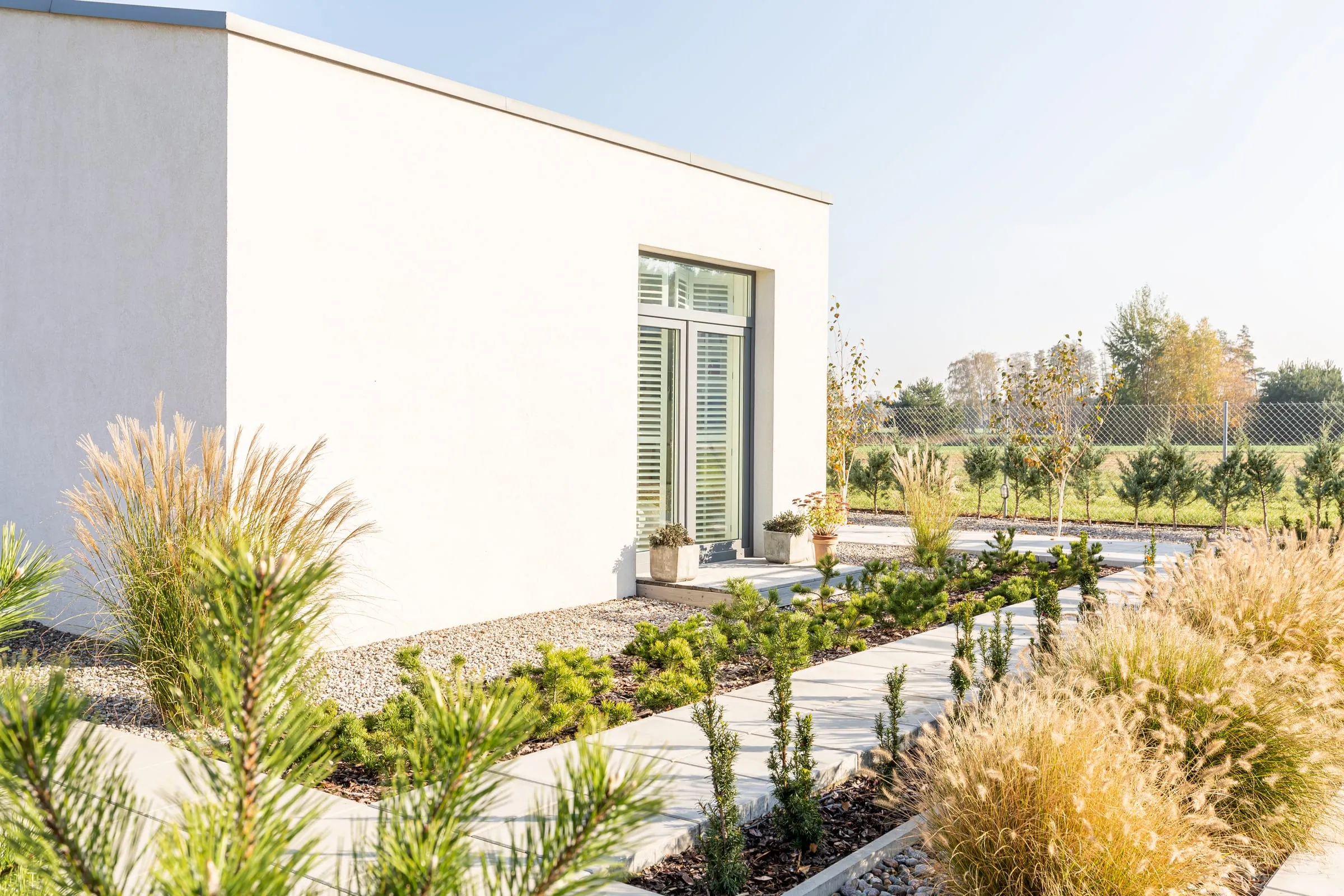Casa moderna blanca con ventanal y jardín de gramíneas