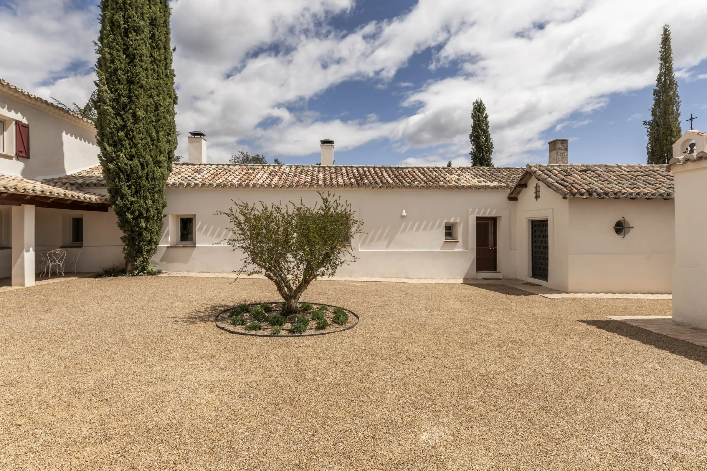 Cortijo de fachadas blancas con patio de grava y un olivo en el centro